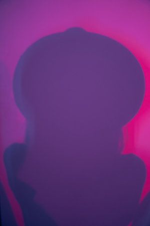A close-up silhouette of a woman in a hat, diffused light. Abstract gradient pink and purple background with a womans shadow. High quality photoの写真素材