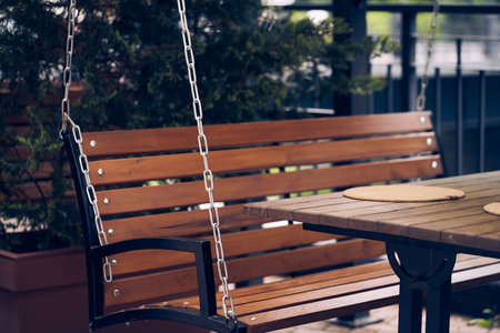 A garden bench seat, a wooden swing bench with a metal chain, with armrests and a backrest, a hanging lounge chair made of solid wood. With space to copy. High quality photoの写真素材