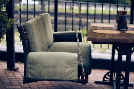 A wooden swing bench is suspended on chains on the summer veranda in the open air. The concept of relaxation. With space to copy. High quality photoの写真素材