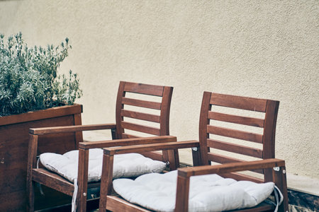Two chairs with soft cushions in the backyard with a green plant in a wooden flowerbed in an open...