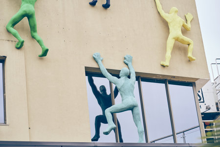 Sculptures of people on the wall. A bright building with an installation in the form of people climbing a wall. The concept of shopping, people are rushing to the sale. High quality photoの写真素材