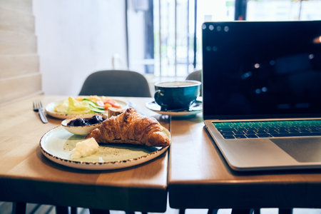 Breakfast is on the desktop, when you are in a hurry, you can eat and work together. Laptop, omelette with vegetables, coffee and croissant with copy space. High quality photoの写真素材