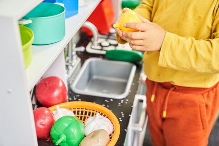An unrecognizable child in a toy kitchen with a sink. Washes plastic vegetables. Educational toys. The concept of healthy eating. Child education and development. High quality photoの写真素材
