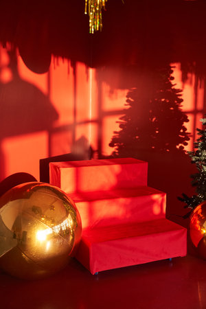 A red ladder on a red background. The shadow of a Christmas tree on the wall. The rooms New Years decor is decorated in red tones. With space to copy. High quality photoの写真素材