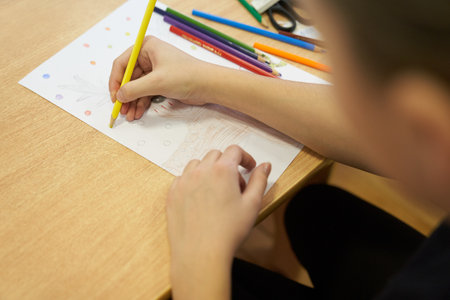 An unrecognizable child is intently drawing on a white sheet at a table with a set of colored pencils. With space to copy. High quality photoの写真素材