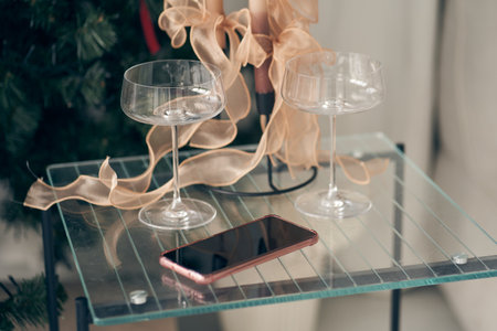 A smartphone with a black screen on the background of a transparent glass table. A festive atmosphere with empty glasses on the table. With space to copy. High quality photoの写真素材