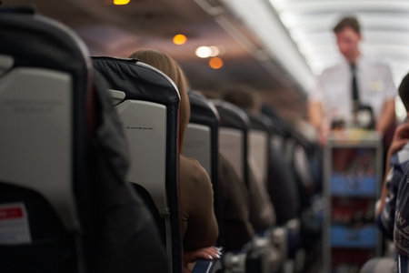 The interior of an airplane with passengers sitting on the seats. A male steward delivers food. Passengers sit along the row on the plane. The concept of travel. High quality photoの写真素材