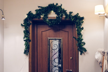 The front door is decorated with a Christmas tree branch with an LED garland on a wire. Festive...