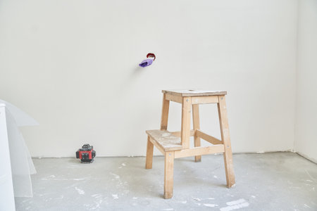 There is a wooden stand next to the laser equipment on the background of a concrete wall. The electrical outlet is unfinished, the wires are rewound with purple electrical tape.の写真素材
