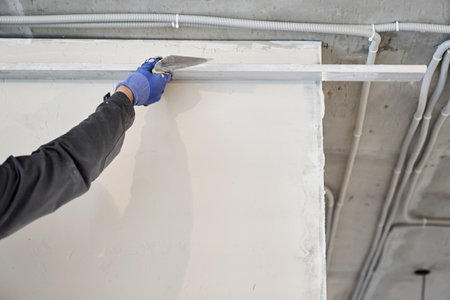 A male plasterer holds a metal rule in his hands and smears plaster on the wall. High quality photoの写真素材