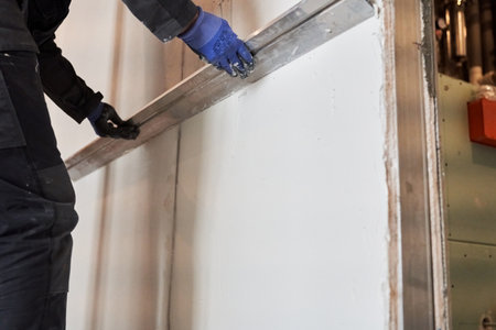 Apartment renovation. Leveling the plastered wall. Home improvement. Mens hands in protective gloves with a building rule. High quality photoの写真素材