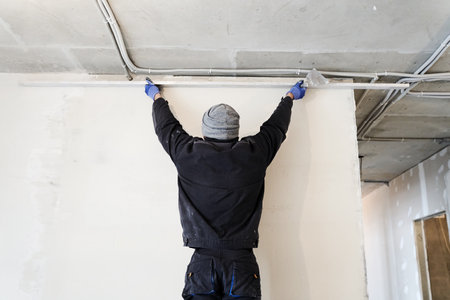 Applying gypsum plaster in a mechanized way to the wall. A worker removes excess plaster using a metal rule. High quality photoの写真素材