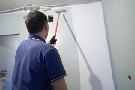 Painting the walls in a vertical line. A man paints concrete walls with a paint roller. Gray paint creates a cozy atmosphere in the room. High quality photoの写真素材