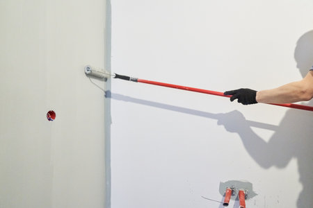 A man paints walls with a roller, working painting on the surface, painting walls in an apartment, repairing with white paint. With space to copy. High quality photoの写真素材