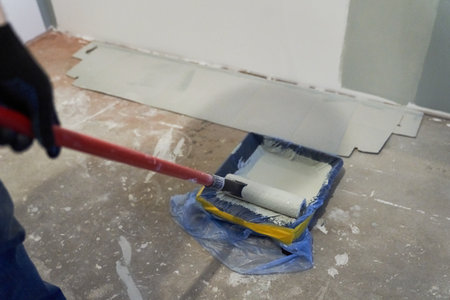 A container of paint for a paint roller. Apartment renovation. Concrete walls are painted gray with a paint roller. High quality photoの写真素材