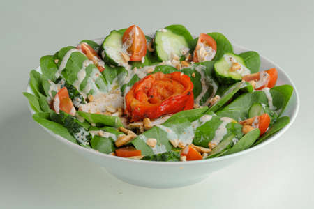 Healthy greens salad with tomato, spinach and nuts on a white plate on a white plateの写真素材