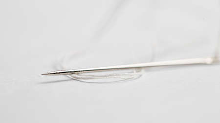 Close-up photo of sewing needles with white thread on white background
