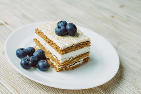 Honey cake with blueberries in a white saucer on the table