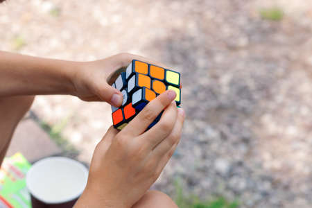 Moscow, July 17, 2021. A boy holds a Rubiks cube puzzle in his hands and collects it in nature, close-up of a childs handsのeditorial素材