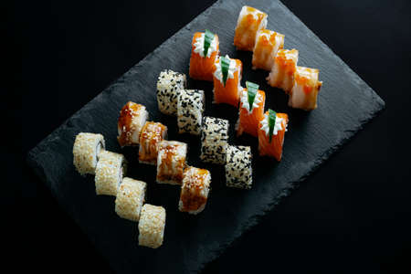 Assorted bright rolls with fish, cheese, eel, perch, caviar and soy unagi sauce on a stone boardの写真素材