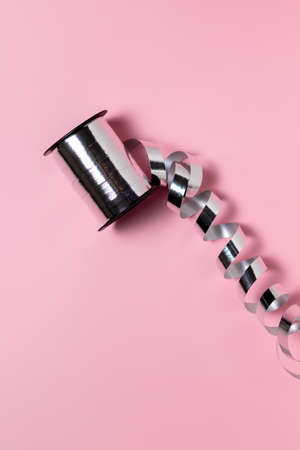 Silver ribbon for wrapping a gift on a solid pink background