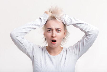 Blonde girl holding her hair on a white background bright emotion in shockの写真素材