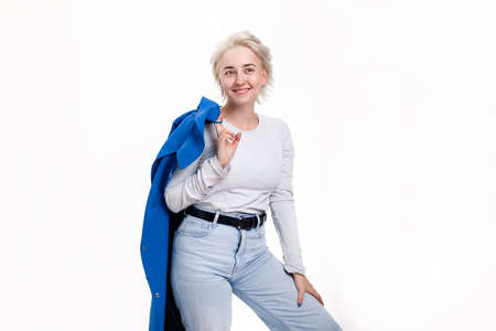 Blonde girl holding a blue coat in her hand smiles broadly on a white backgroundの写真素材