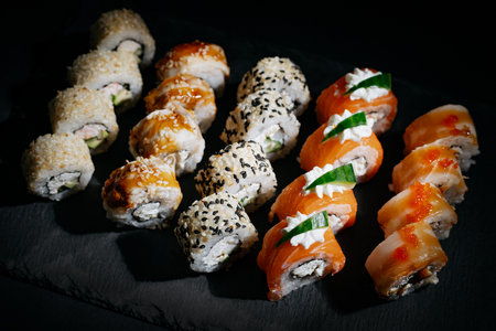 Assorted bright rolls with fish, cheese, eel, perch, caviar and soy unagi sauce on a stone boardの写真素材