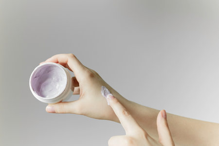 Womans hand is using her finger to apply a smear of organic cream from a jar to her other hand.の写真素材