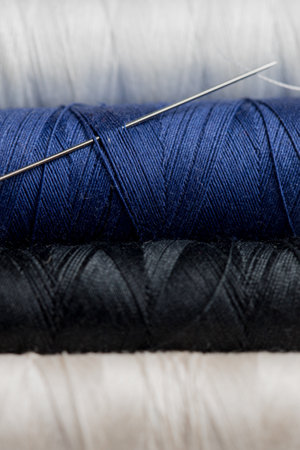 Macro photo of thread for sewing on a spool of black white and blue color with a needleの写真素材
