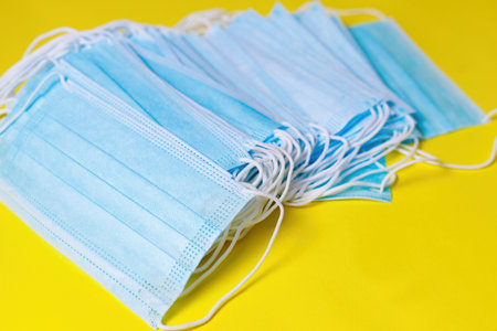 Many blue medical masks on yellow backgroundの写真素材