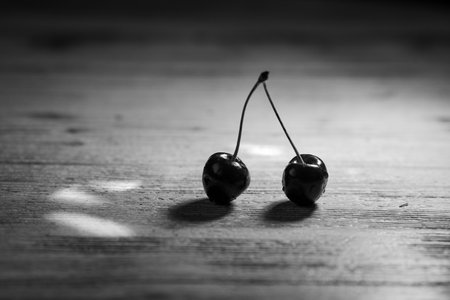 Ripe red cherries lie on the table in the rays of light on a dark background. Black and white photoの写真素材