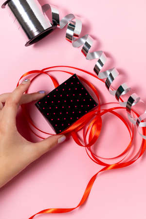Close-up of a hand holding a small gift box on a solid pink background, where the ribbons for packaging lieの写真素材