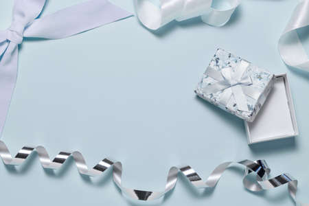 Small gift box with bow, blue and silver ribbons for gift wrapping on a blue backgroundの写真素材