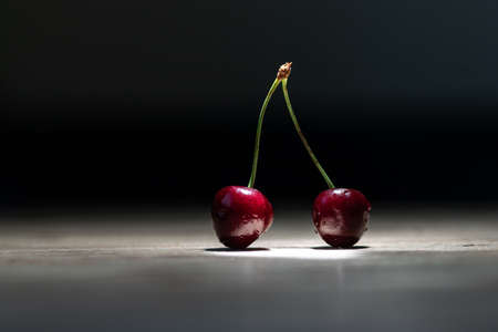 Ripe red cherries lie on the table in the rays of light on a dark backgroundの写真素材