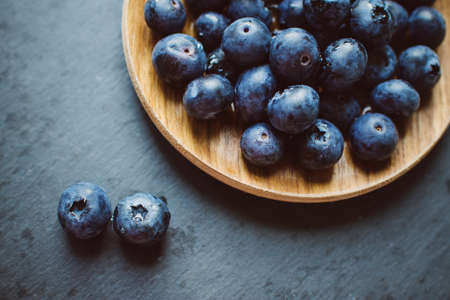 Fresh ripe blueberry in a wooden bowl over dark slate, stone or concrete background.