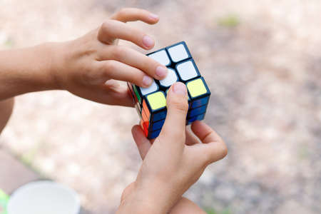Moscow, July 17, 2021. A boy holds a Rubiks cube puzzle in his hands and collects it in nature, close-up of a childs handsのeditorial素材