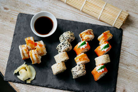 Assorted bright rolls with fish, cheese, eel, perch, caviar and soy unagi sauce on a stone boardの写真素材