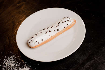 Dessert eclair with cream on a white plate on the table. Sugar. Junk food