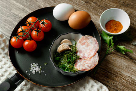 Ingredients for fried eggs in a pan: eggs, herbs, garlic, cherry tomatoesの写真素材