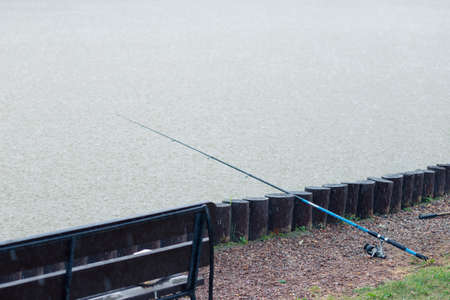 The fishing rod lies on a stone bank, lowered into the water and waits for the fish to bite during heavy rainの写真素材