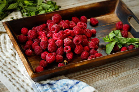 A lot of ripe raspberries on a tray after picking, lies on a wooden table with a mint and a tea towelの写真素材