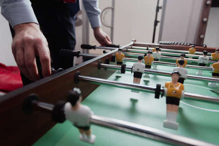A man in the office plays table football. Little toy players in yellow and white uniformsの写真素材