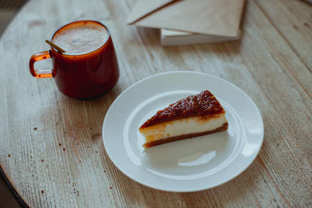 Coffee in a glass cup and nutty cheesecake on a white plate stand on a wooden table. High quality photoの写真素材