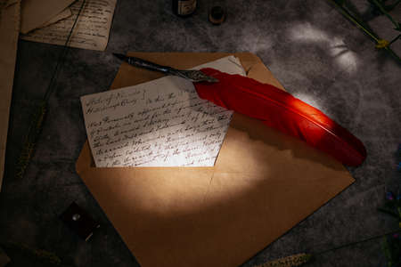 Paper letters, craft carpet, quill, inkwell and flowers lie on the table. Bright sunny day. View...