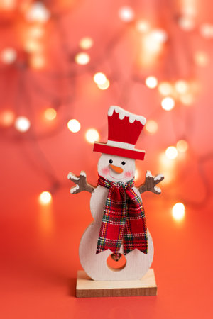 Figurine of a cheerful cute snowman on a red christmas background, glowing bokehの写真素材