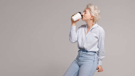 Blonde girl holding a plastic cup with a drink in her hands on a light background. High quality...