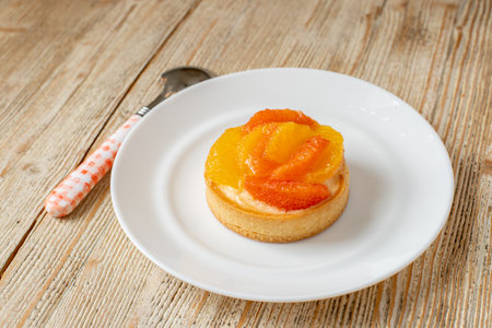 Tartlet with tangerine and grapefruit lies on a plate on a wooden table. beautiful dessertの写真素材