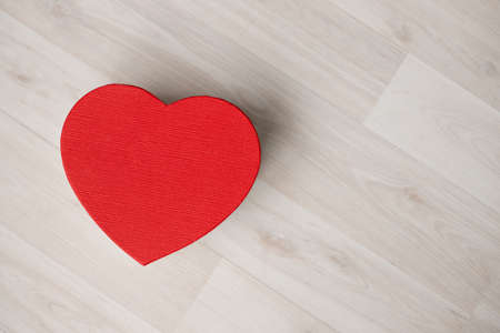 A gift box in the form of a red heart stands on a wooden floor. Valentines Day - February 14の写真素材