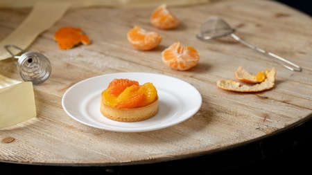 Tartlet with tangerine and grapefruit lies on a plate on a wooden table. beautiful dessert. high quality photoの写真素材